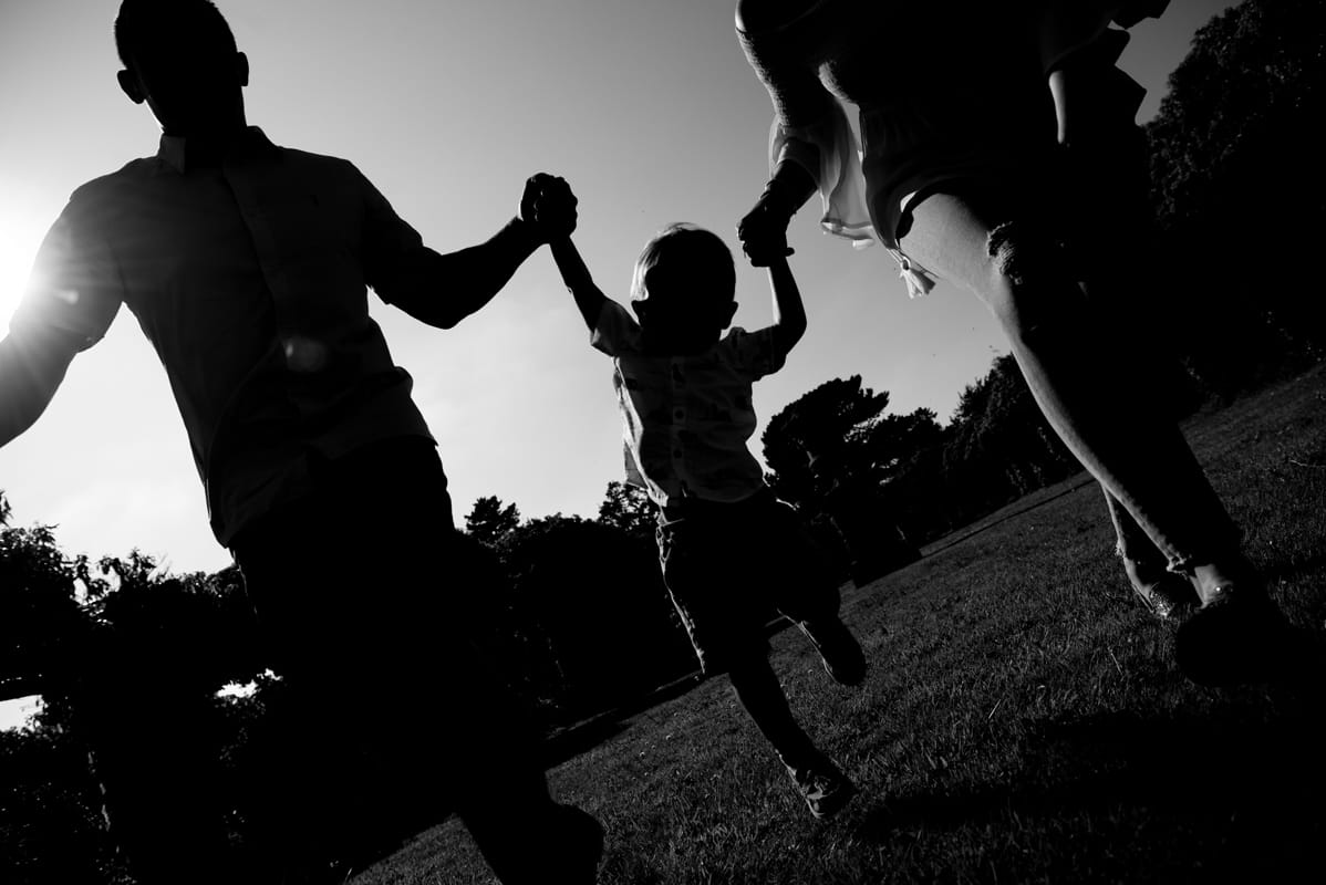 family running and swinging child by arms with sun behind